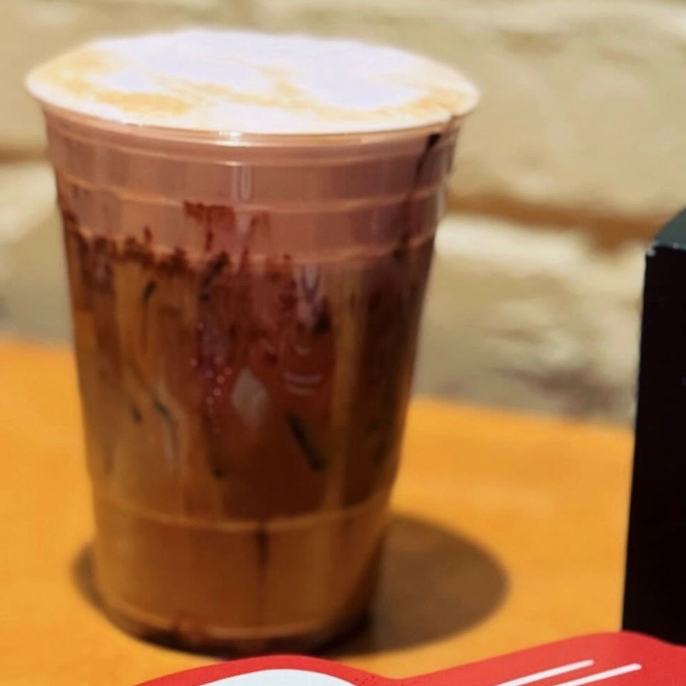 An iced mocha with chocolate drizzle on the table by the brick wall