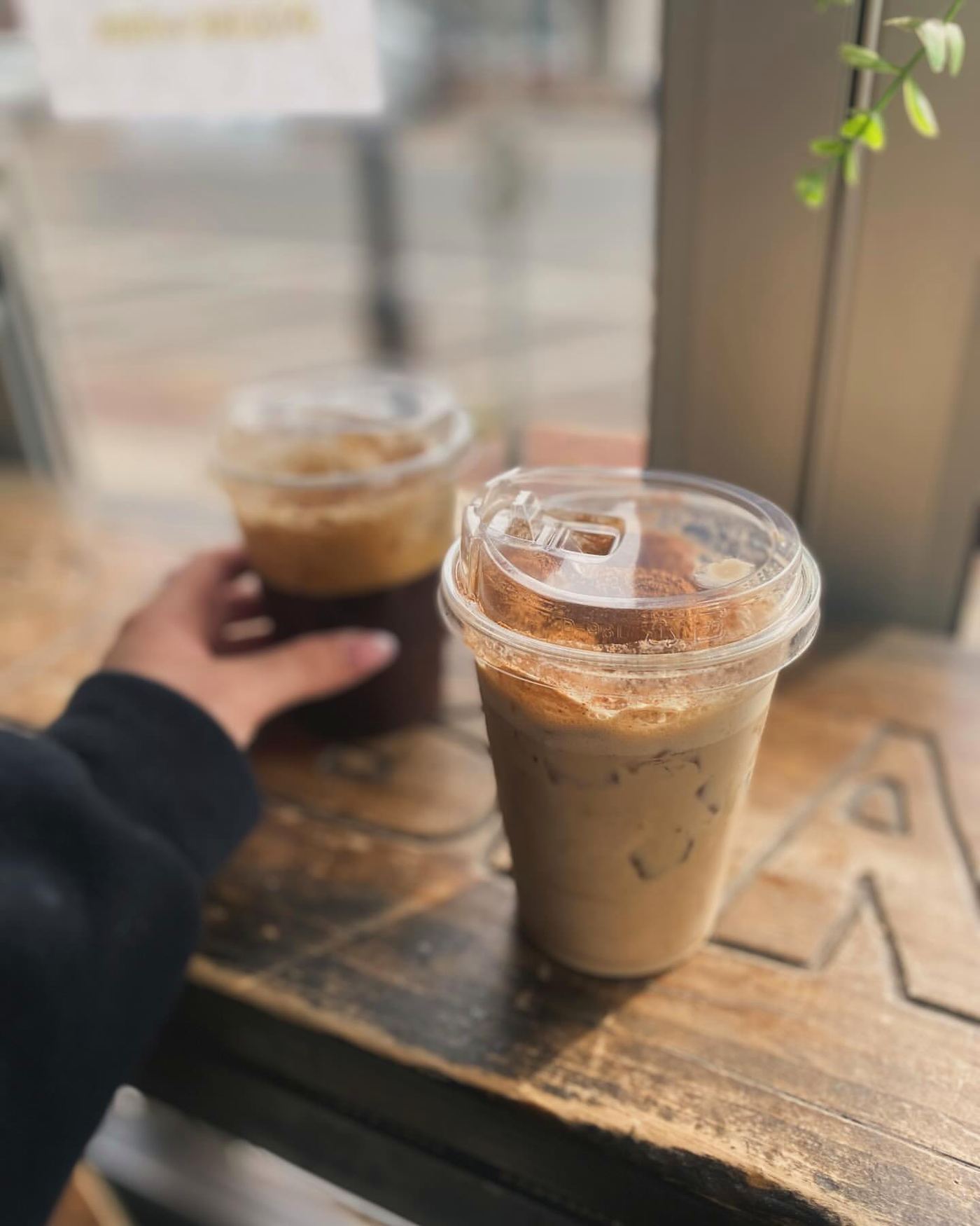Two iced coffees on the wooden table by the front window